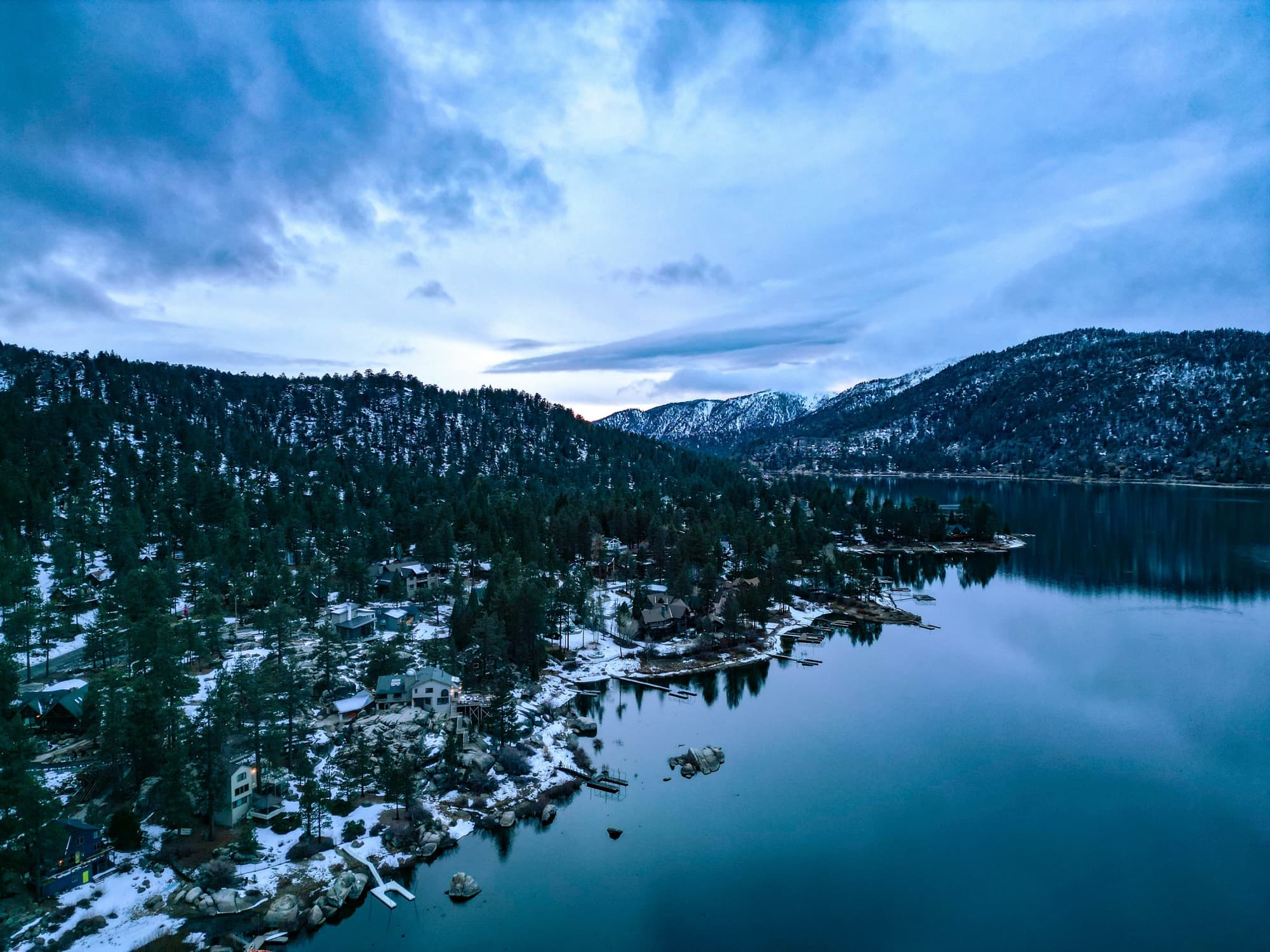 Aerial view of Big Bear Lake surrounded by snow-capped mountains and pine forests
